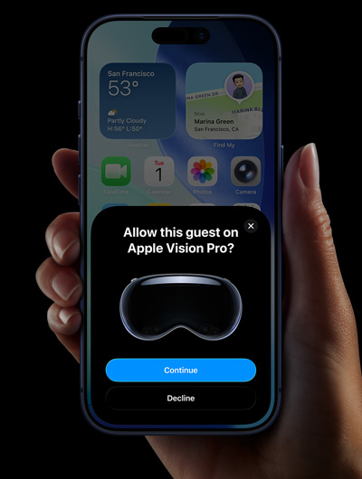 A hand holding an iPhone, the iPhone screen displays a window with the message: Allow this guest on Apple Vision Pro with buttons labelled: Continue and Decline