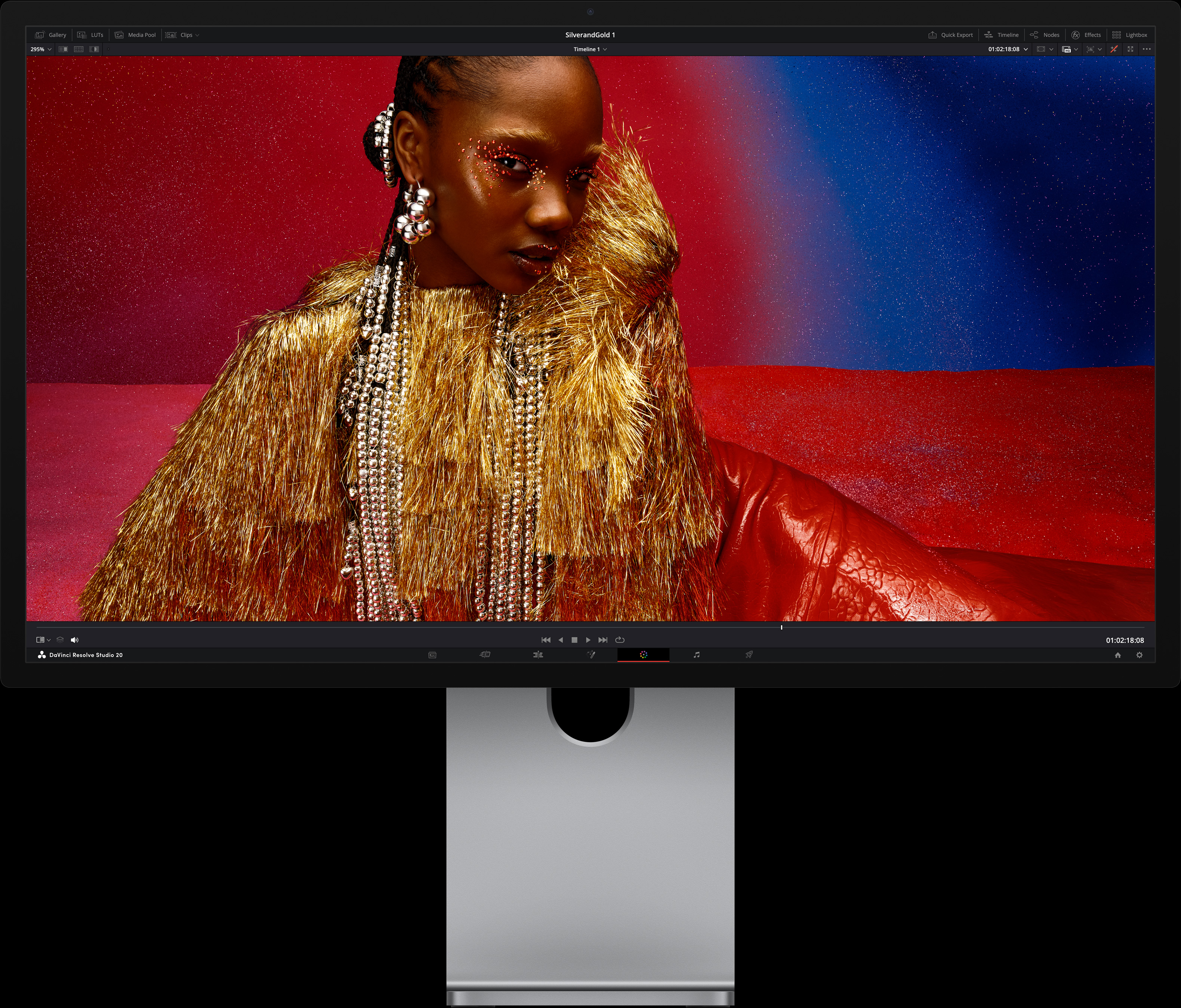 Osoba u jarkocrvenoj haljini s predimenzioniranim metalik modnim dodacima sjedi ispred pozadine s plavim i crvenim gradijentom, prikazujući kvalitetu slike dostupnu na zaslonu Studio Display XDR