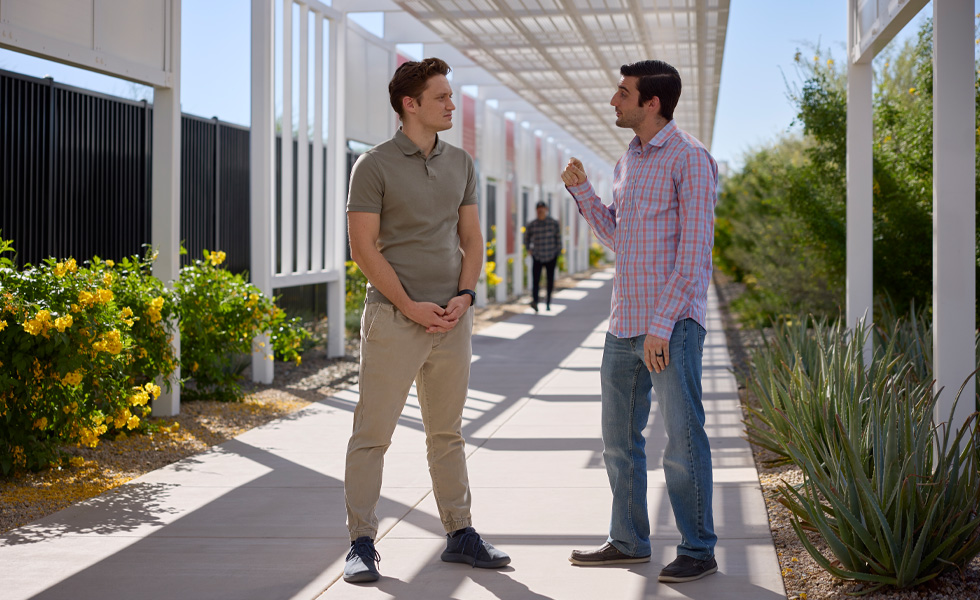 Two casually dressed employees speak under a covered walkway